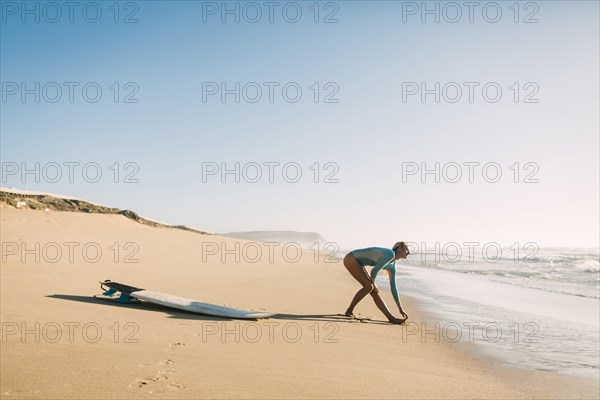 Woman wearing wetsuit stretching on beach