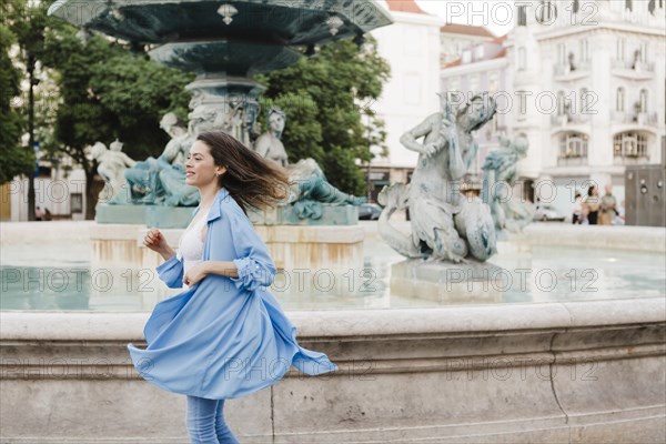 Woman wearing blue coat turning by fountain