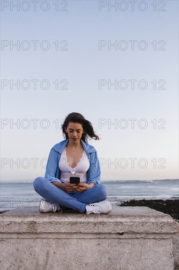 Woman using phone sitting on wall