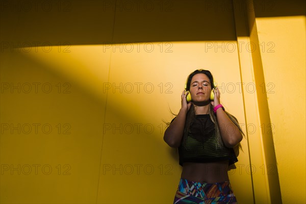 Woman wearing headphones by yellow wall