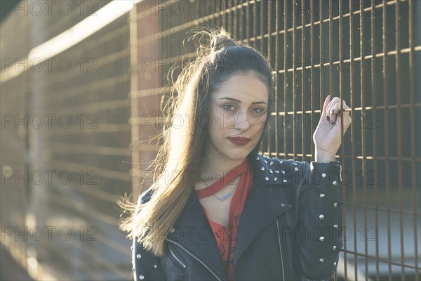 Woman wearing leather jacket holding metal fence