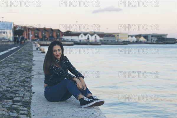 Woman sitting on footpath by sea in Lisbon, Portugal