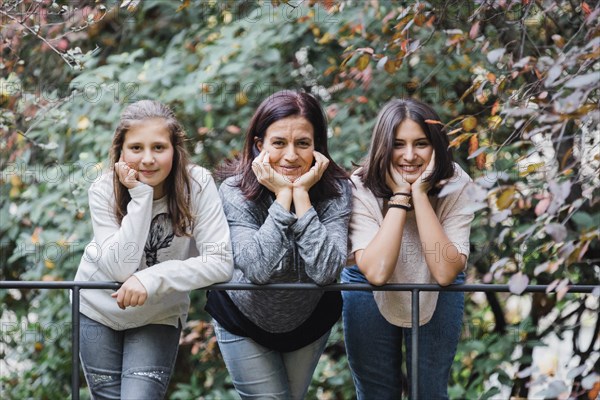 Mother and daughters smiling and  leaning on railing