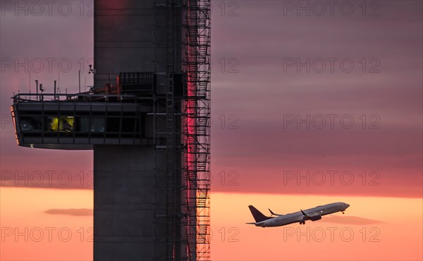 Airplane flying past control tower at sunset