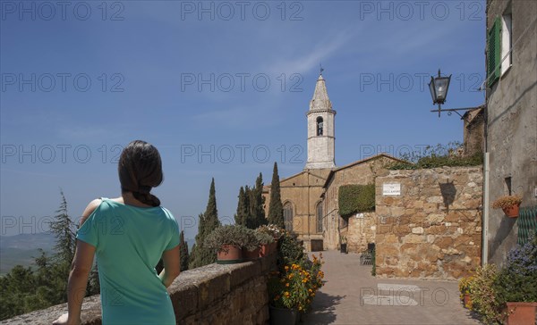 Woman by stone wall and church in Tuscany, Italy