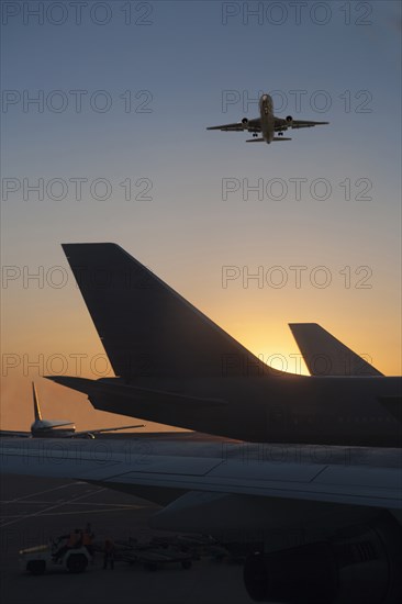 Airplane flying over airplane on runway at sunset