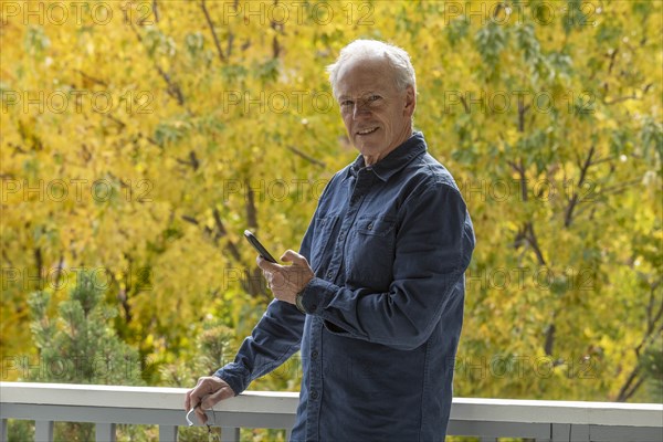 Smiling man holding phone by autumn trees