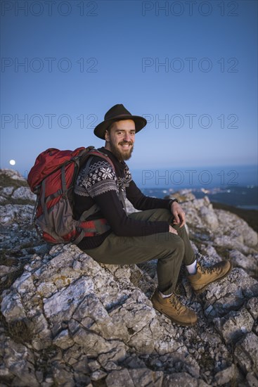 Smiling man sitting on rock at sunset
