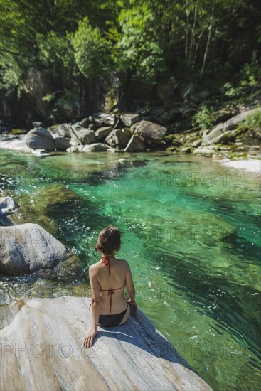 Woman wearing bikini sitting on rock by river