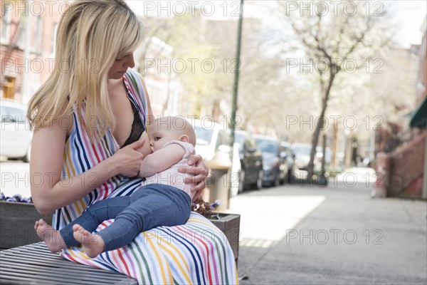 Mother breastfeeding her daughter on city bench