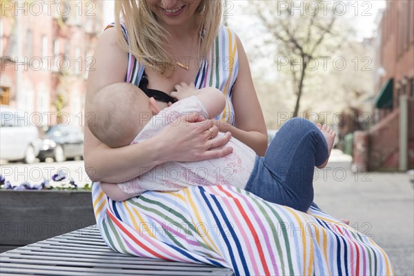 Mother breastfeeding her daughter on city bench