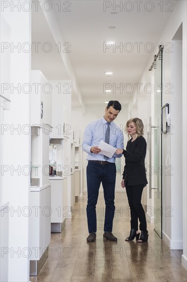 Dentist and dental nurse discussing notes in corridor
