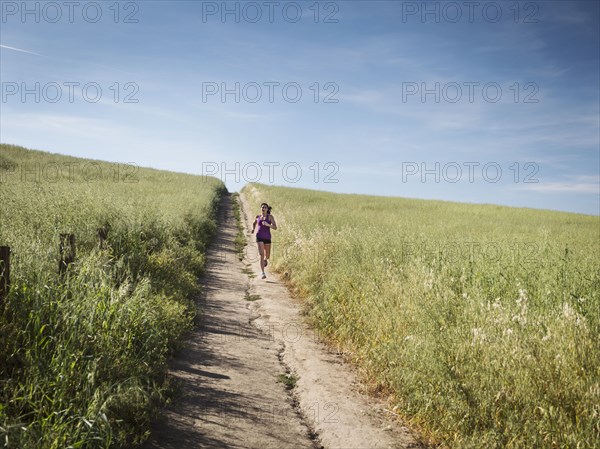 Mid adult woman jogging on path through field