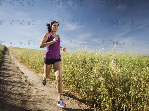 Mid adult woman jogging on path through field