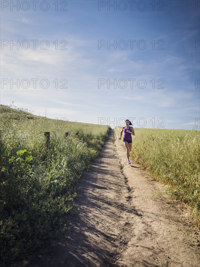 Mid adult woman jogging on path through field