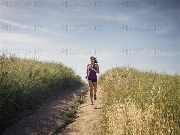 Mid adult woman jogging on path through field