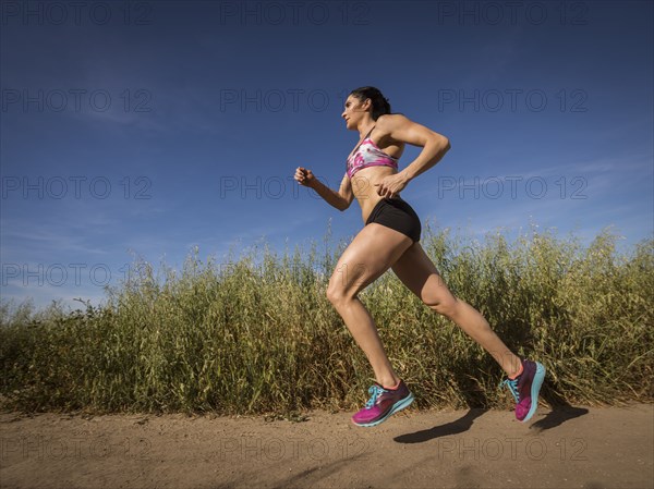 Mid adult woman jogging on path through field