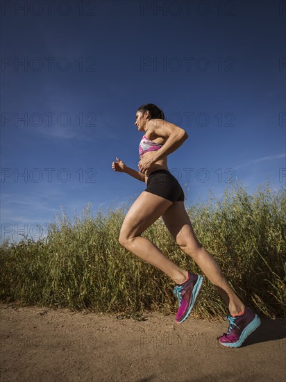 Mid adult woman jogging on path through field