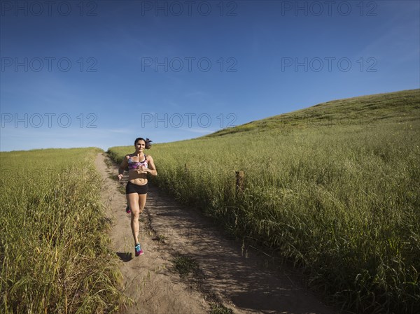 Mid adult woman jogging on path through field