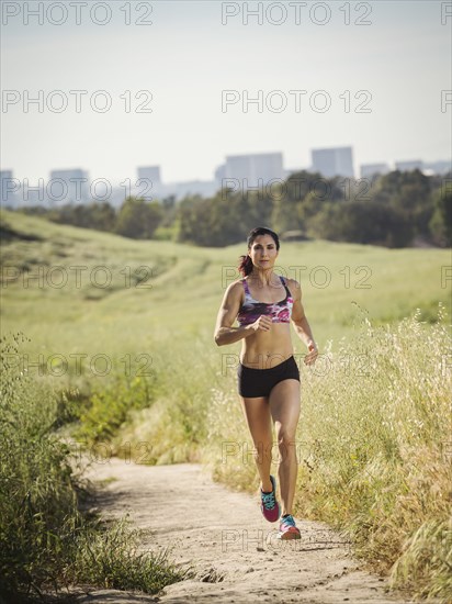 Mid adult woman jogging on path through field