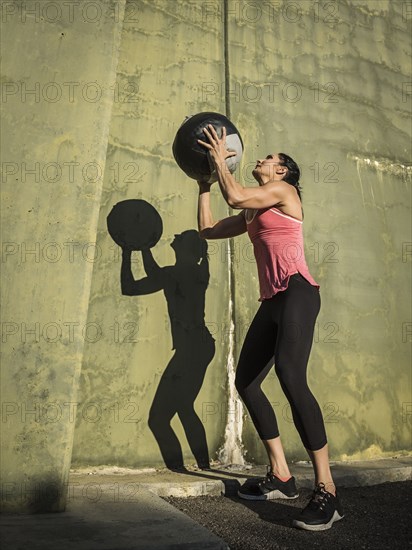 Woman throwing medicine ball against concrete wall