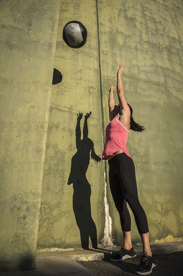 Woman throwing medicine ball against concrete wall