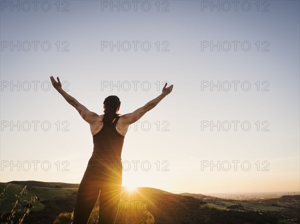 Rear view of woman with arms raised at sunset