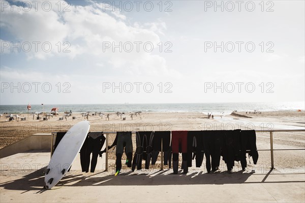 Wetsuits and surfboard on railing at Carcavelos Beach