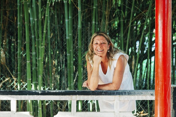 Smiling woman leaning on fence by bamboo