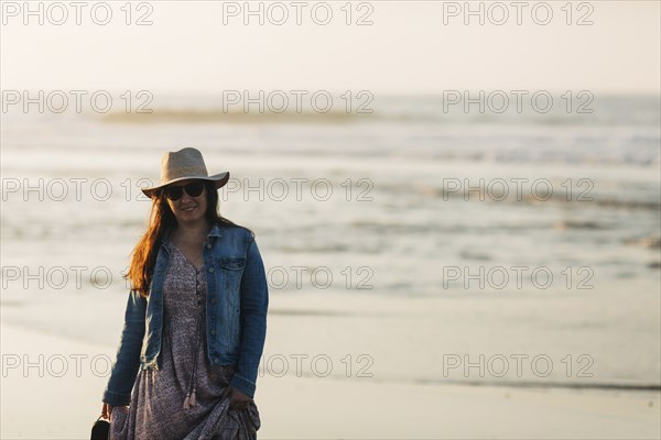 Woman in sunhat and denim jacket on beach