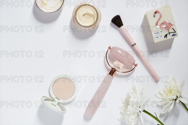 Facial roller, make-up and flowers on white table