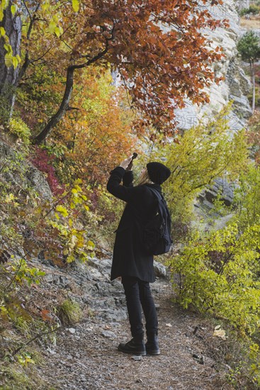 young woman photographing with smartphone in autumn forest