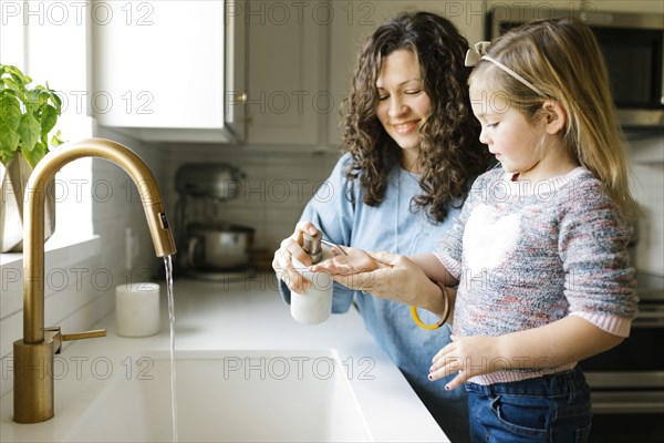 Mother and daughter washing hands in kitchen sink