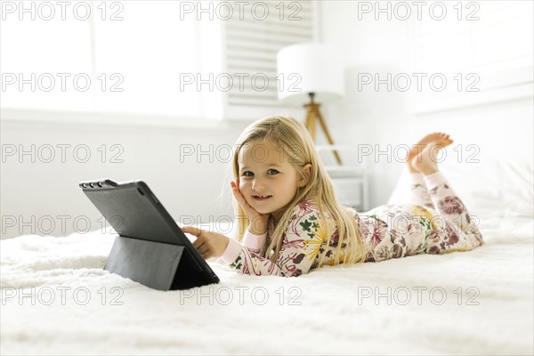 Girl in pajamas using digital tablet while lying on bed