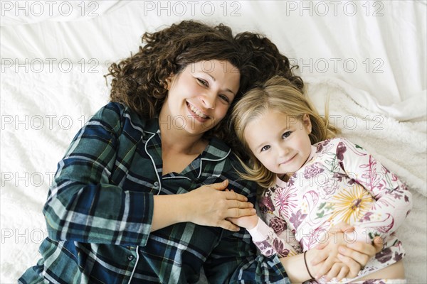 High angle view of mother and daughter in pajamas lying on bed