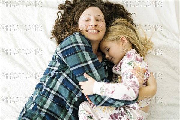 High angle view of mother and daughter in pajamas lying on bed
