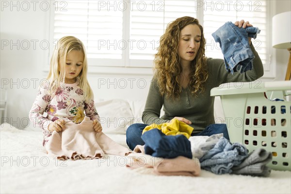 Mother and daughter folding laundry on bed