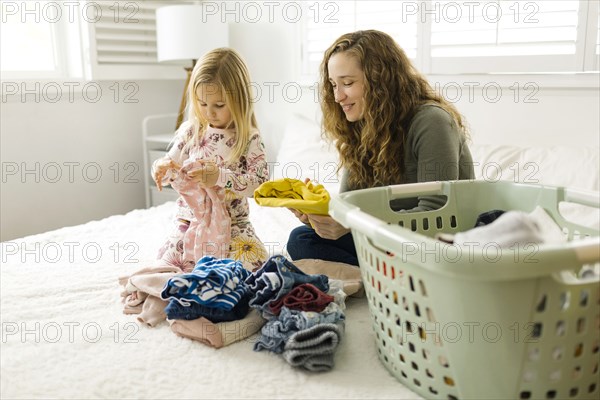 Mother and daughter folding laundry on bed
