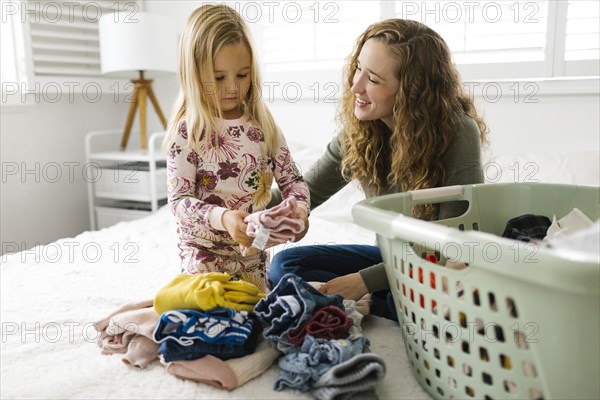 Mother and daughter folding laundry on bed