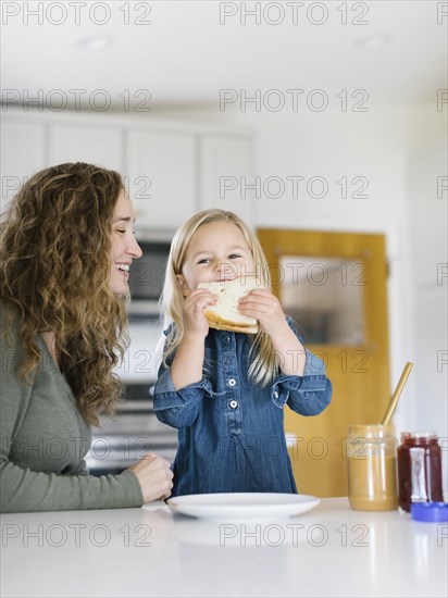 Smiling woman watching daughter eat sandwich