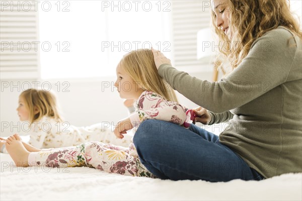 Woman brushing her daughter's hair on bed