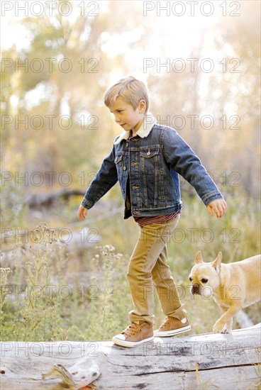 Boy and pet French bulldog walking on fallen tree