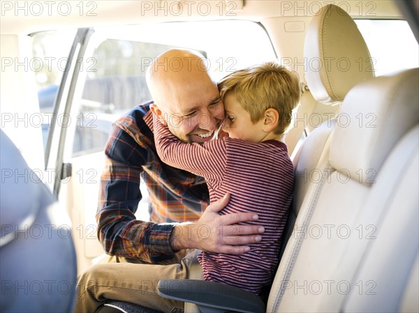 Boy sitting in car hugging his father