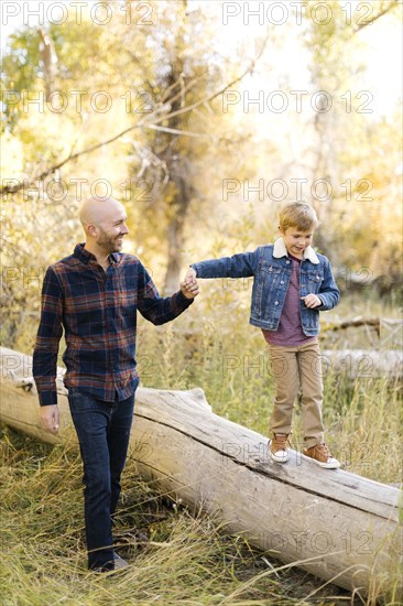 Man holding son's hand as he walks on fallen tree