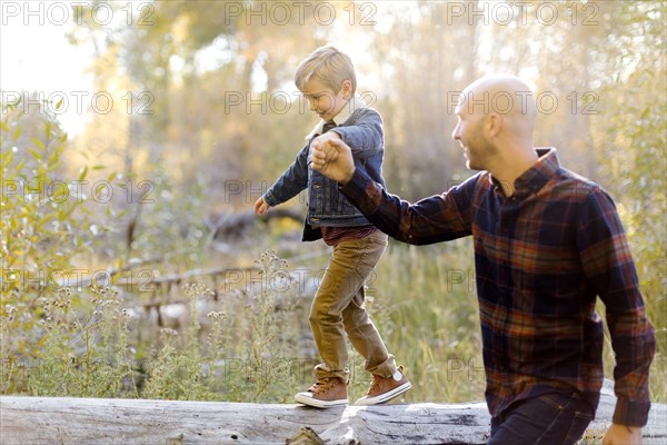 Man holding son's hand as he walks on fallen tree