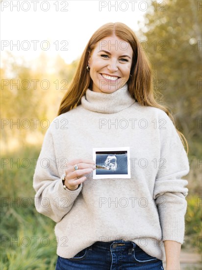 Smiling pregnant woman holding ultrasound photograph