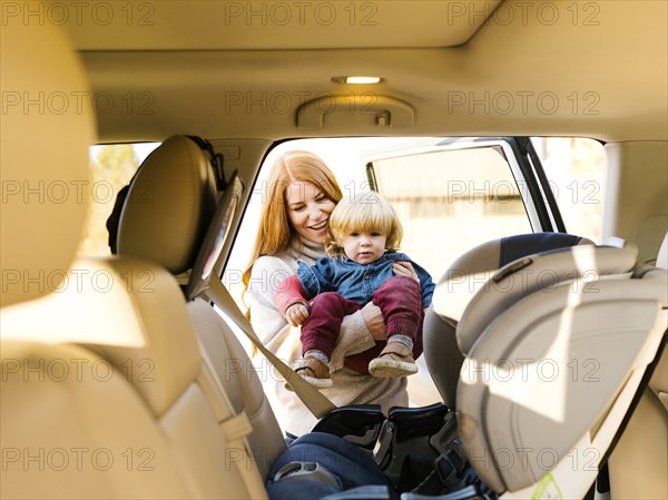 Smiling woman carrying son into car seat