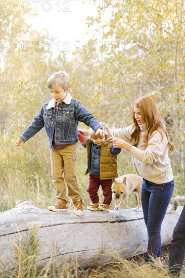 Woman holding hands of her sons as they walk on fallen tree