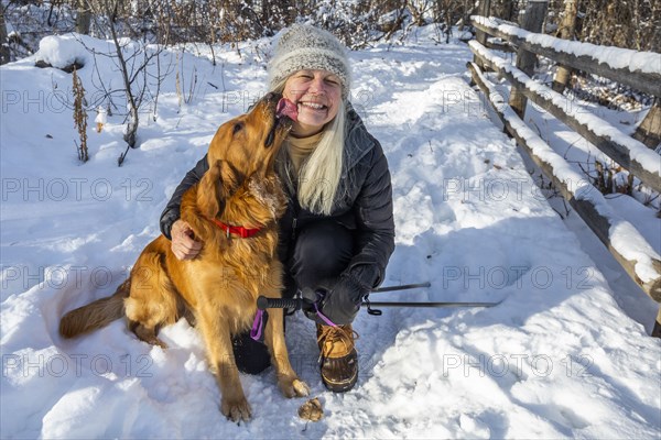 Smiling senior woman petting dog in snow