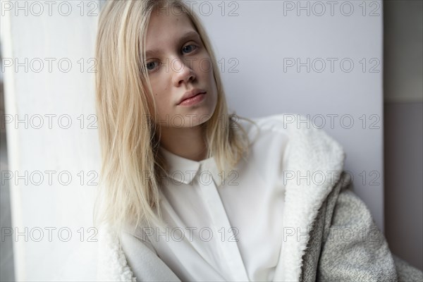 young woman in wool coat leaning against wall